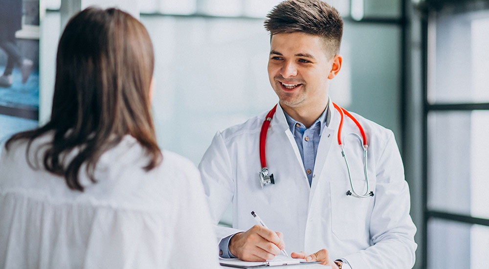 Happy doctor with stethoscope writing prescription for patient