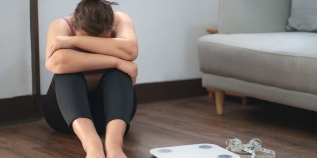 Frustrated woman sitting near weight scales at home