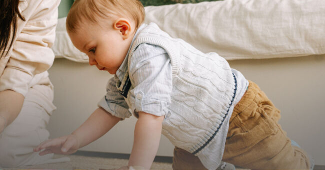 Toddler playing with large wooden blocks under parent supervision in a safe home setting.