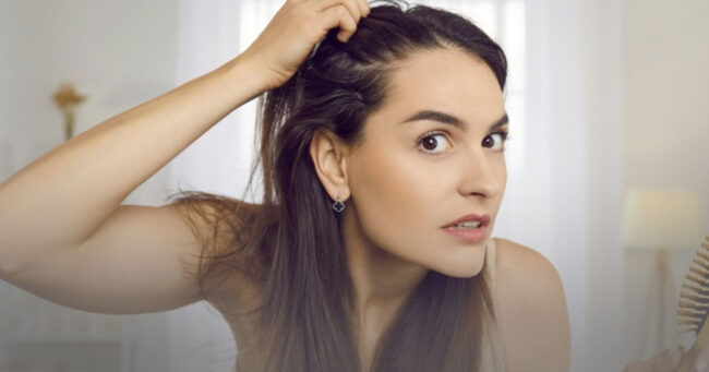 Woman gently examining her hairline at home, representing early awareness of hair thinning and hair loss concerns.