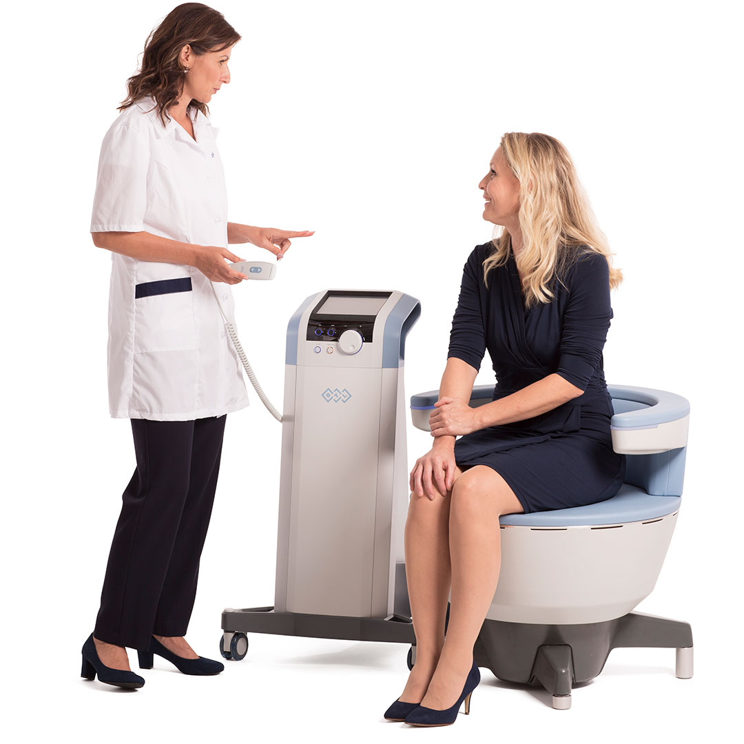 Healthcare professional explaining EMSELLA pelvic floor therapy to a woman seated on the treatment chair.